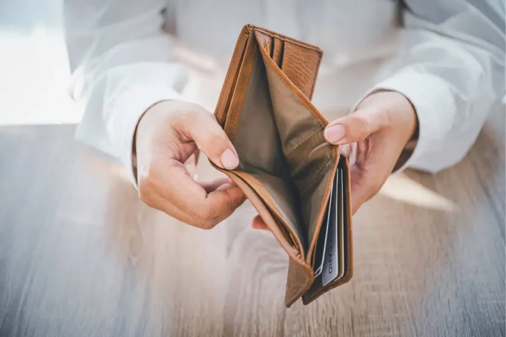 a women opening an empty brown wallet, showing there is no money inside
