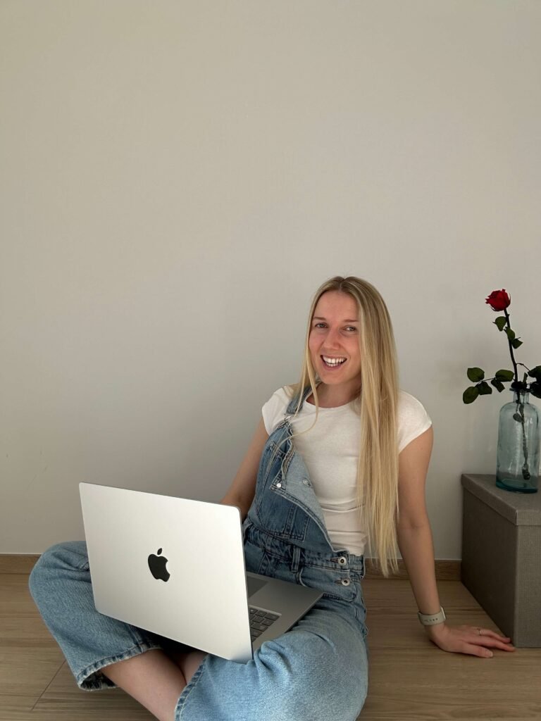 Klaudia sitting on the floor with laptop on her legs and similing